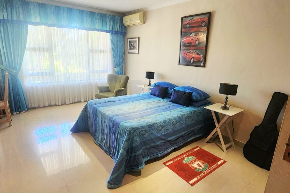 A spacious bedroom featuring built-in cupboards, tiled flooring, and an air conditioning unit, offering a comfortable and functional living space.