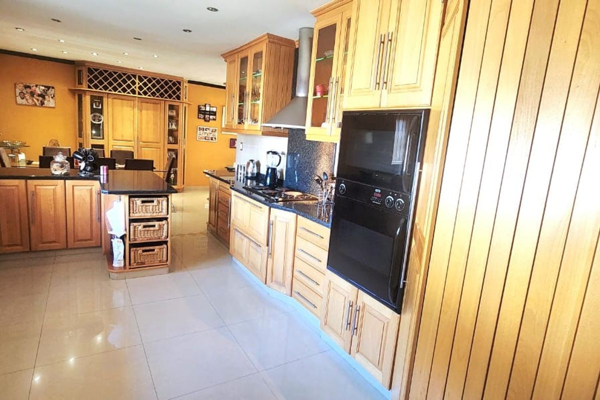 Spacious kitchen featuring extensive wooden cabinetry, granite countertops, built-in oven, and integrated hob, flowing into an open-plan dining area with tiled flooring.