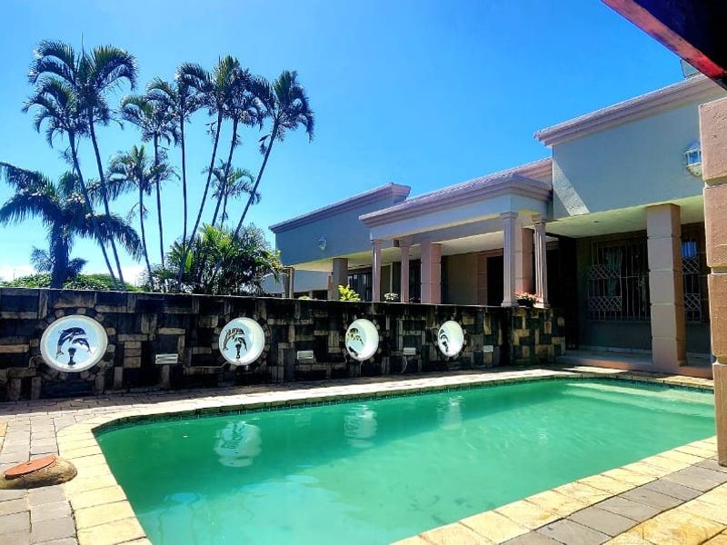 Outdoor pool area featuring a paved patio, covered entertainment space, and a decorative stone wall with integrated circular accents.