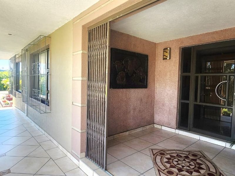 A covered patio area featuring tiled flooring, security gates, and a glass entrance door, providing a secure and functional outdoor transition space.