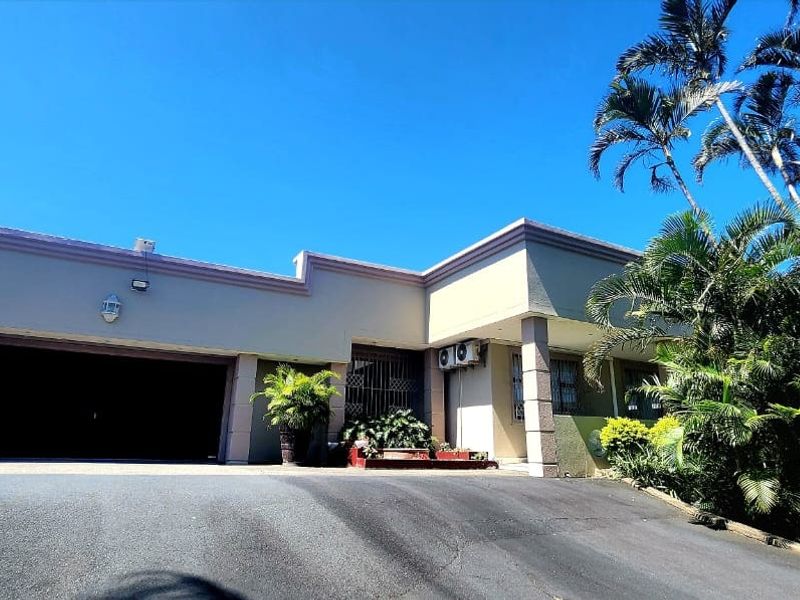 Front elevation of the property featuring a double garage, paved driveway, and established tropical landscaping.