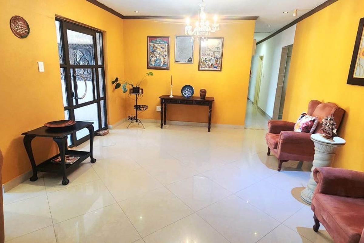 Spacious living area featuring bright yellow walls, polished tiled flooring, and a decorative chandelier, providing a warm and inviting atmosphere.