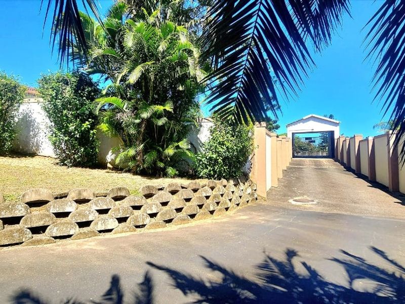 A paved driveway leading to a secure garage, featuring a retaining wall and perimeter boundary walls with established garden landscaping.
