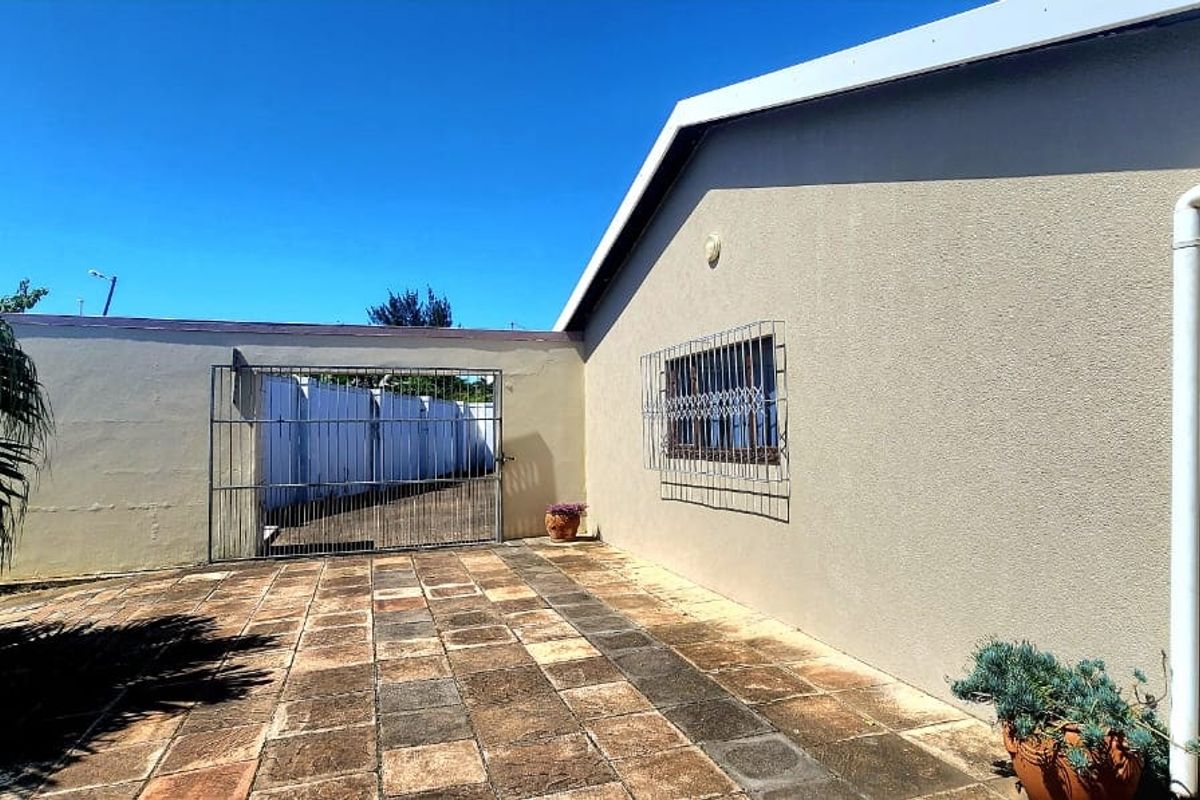 A paved rear courtyard area featuring a security gate, boundary wall, and exterior wall with security bars on the window.