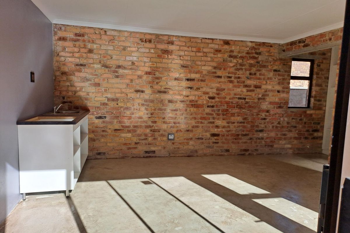 An unfinished kitchen area featuring an exposed brick wall, concrete flooring, and a basic sink unit, offering a blank canvas for renovation.
