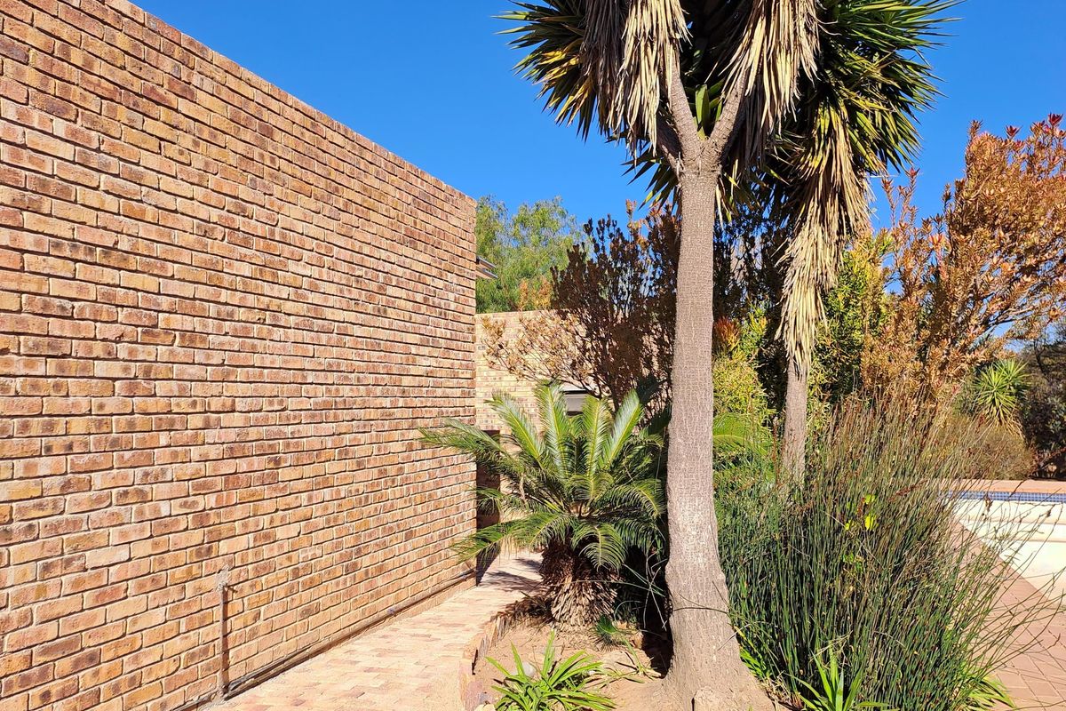 A view of the rear exterior featuring a face brick wall, brick paved pathway, and established garden landscaping.