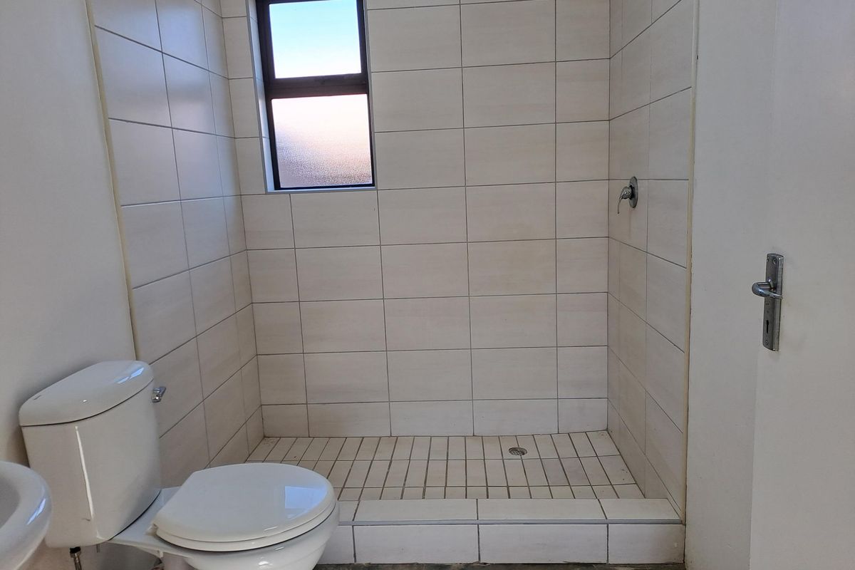 A functional bathroom featuring a tiled shower enclosure, toilet, and obscured glass window, currently awaiting final floor finishing.