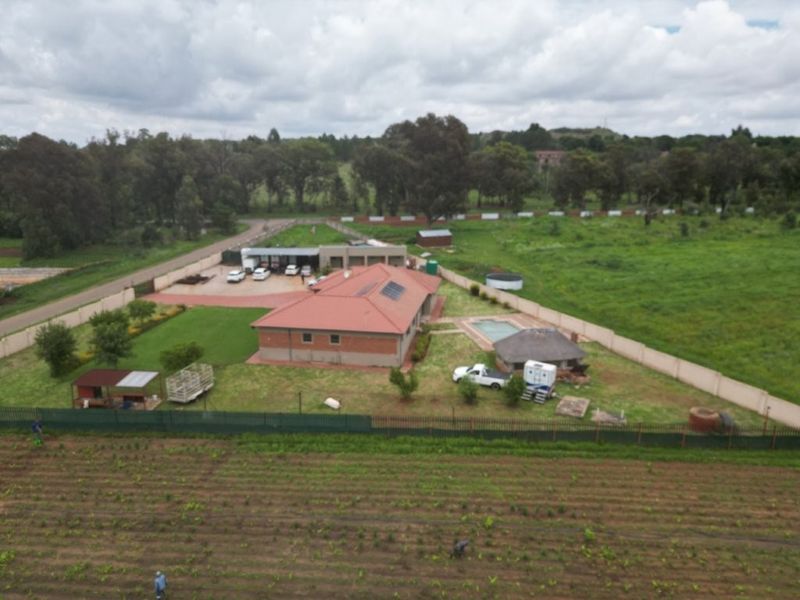 Aerial view of a residential property featuring a main house with solar panels, a swimming pool, a thatched lapa, and extensive surrounding grounds.