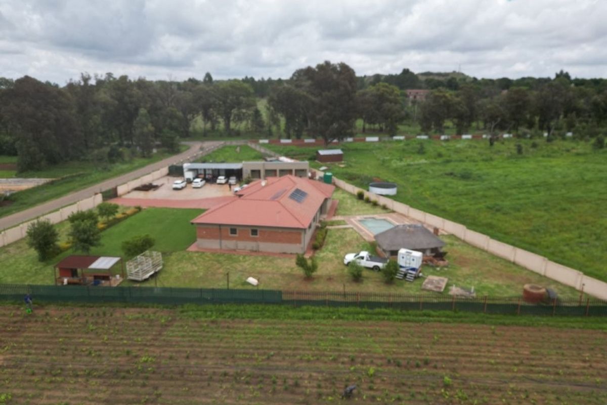 Aerial view of a residential property featuring a main house with solar panels, a swimming pool, a thatched lapa, and extensive surrounding grounds.
