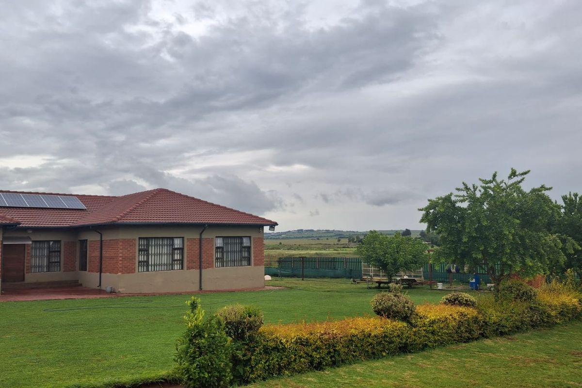 Rear view of a brick house featuring a tiled roof with solar panels, security bars on windows, and a well-maintained lawn and garden area.