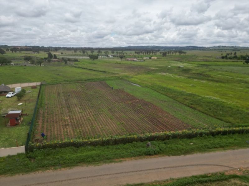 An aerial view of a large plot of land featuring cultivated soil and perimeter fencing, situated in a rural or semi-rural landscape.
