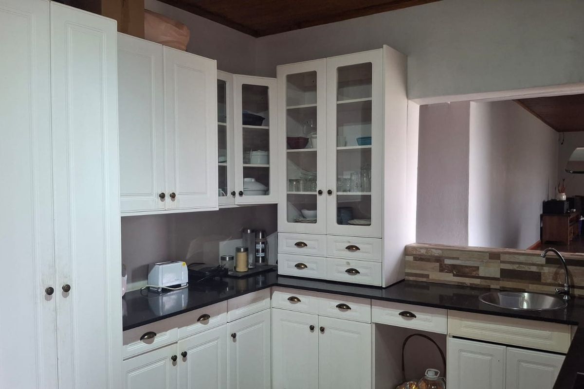 A functional kitchen featuring white cabinetry, dark stone countertops, a tiled backsplash, and a convenient pass-through window to the adjacent living area.