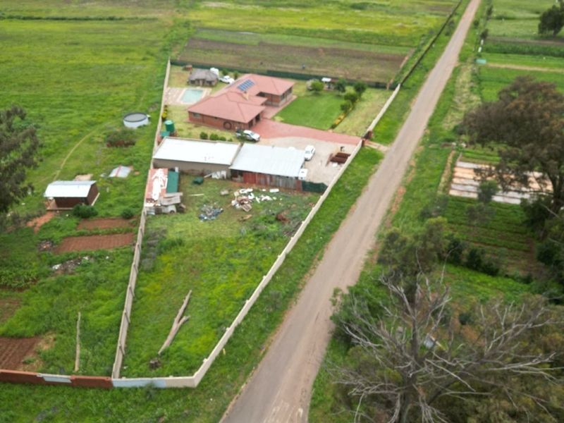 Aerial view of a residential property featuring a main house, swimming pool, outbuildings, and a large plot of land enclosed by perimeter walls.