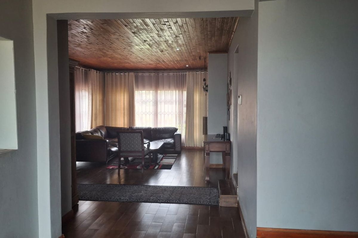 Spacious living area featuring warm timber ceilings, dark laminate flooring, and large windows with natural light.