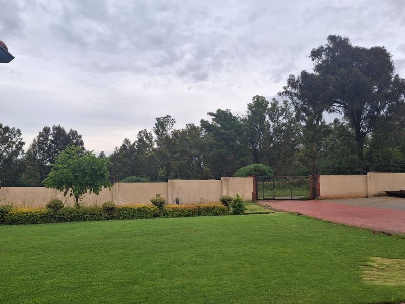 A spacious garden area featuring a well-maintained lawn, perimeter walling, and a gated entrance with a paved driveway.