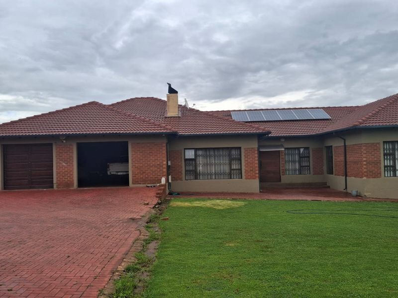 Front view of a single-story brick house featuring a double garage, paved driveway, solar panels, and a well-maintained lawn.