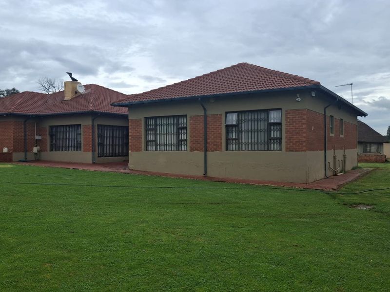 Rear view of a single-story brick house featuring a tiled roof, security bars on windows, and a surrounding lawn area.