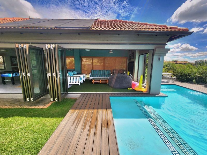 Covered patio area featuring folding glass doors, timber decking, and direct access to a swimming pool with solar roof panels.