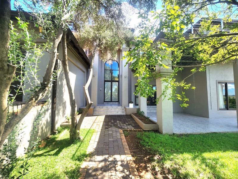 Front entrance of the house featuring a paved walkway, covered patio area, and a striking double-height arched window.