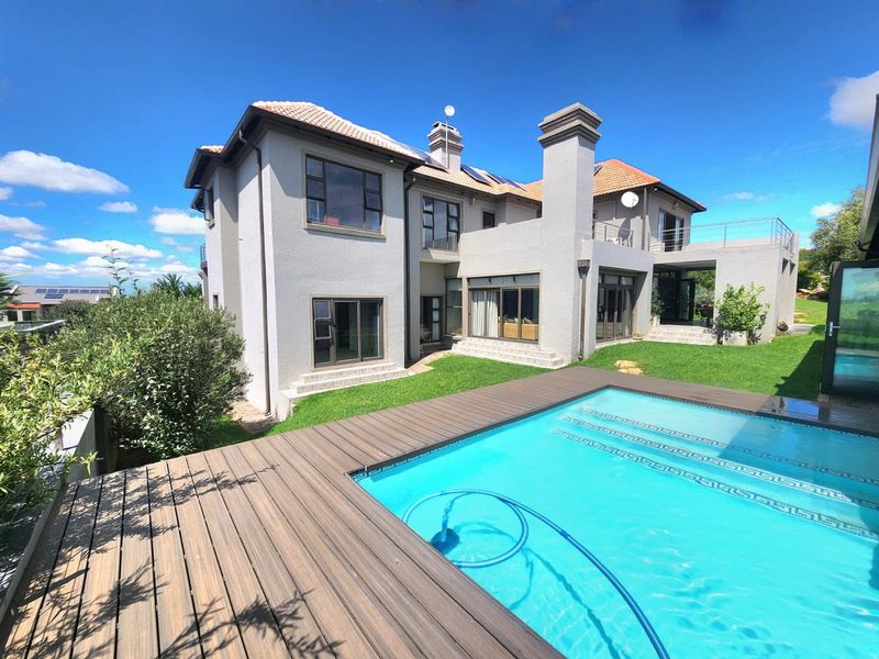 Rear view of a multi-story house featuring a swimming pool, timber decking, a terrace, and a balcony with solar panels on the roof.