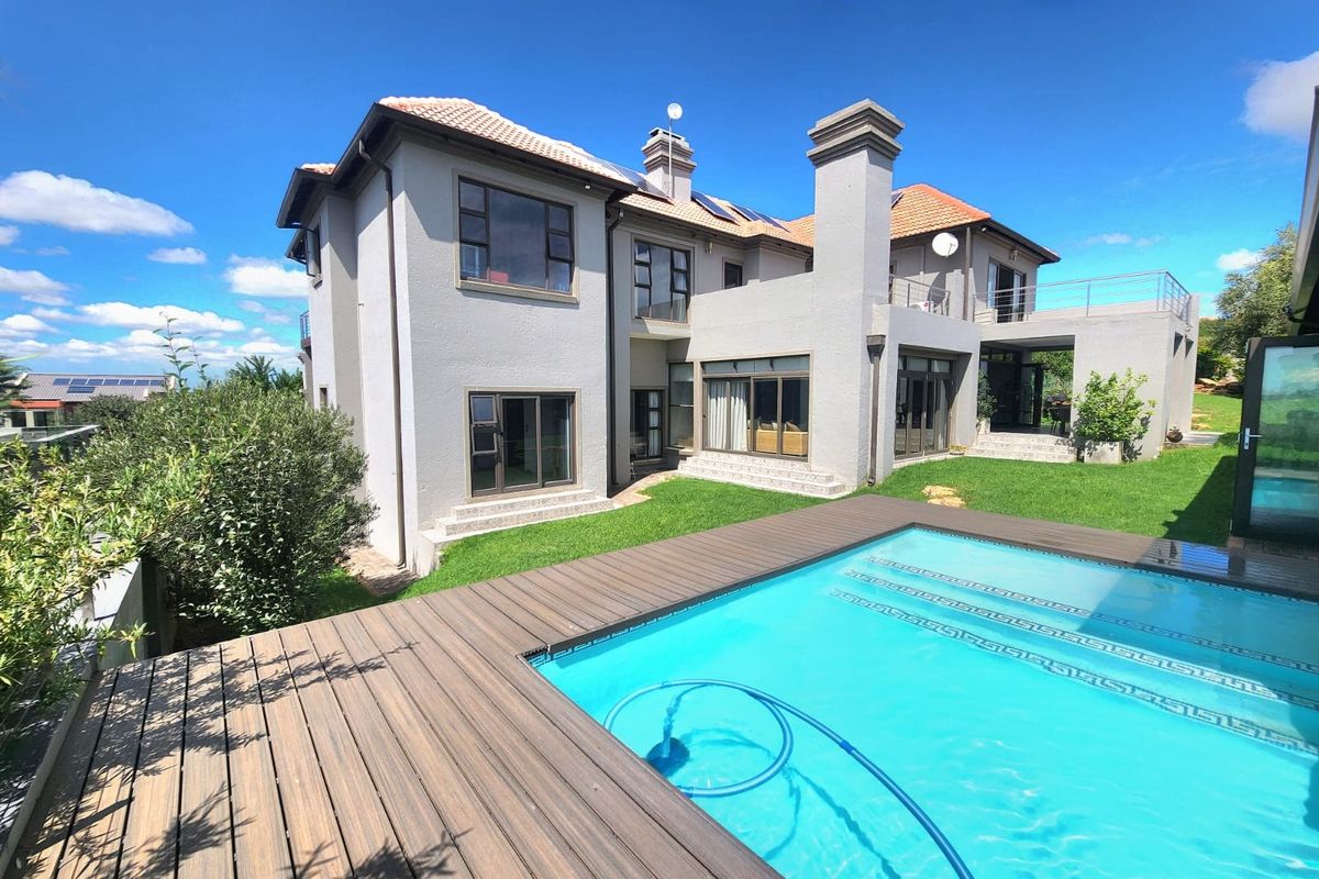 Rear view of a multi-story house featuring a swimming pool, timber decking, a terrace, and a balcony with solar panels on the roof.