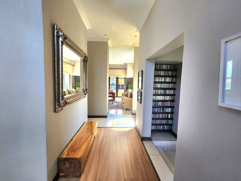 A bright and well-maintained hallway featuring laminate flooring, recessed downlighting, and a built-in shelving unit, leading towards an open-plan living area.
