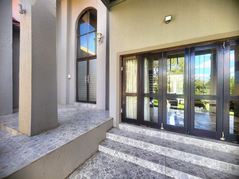 Covered patio area featuring patterned ceramic tiling, arched glass entrance, and folding glass doors providing seamless indoor-outdoor flow.