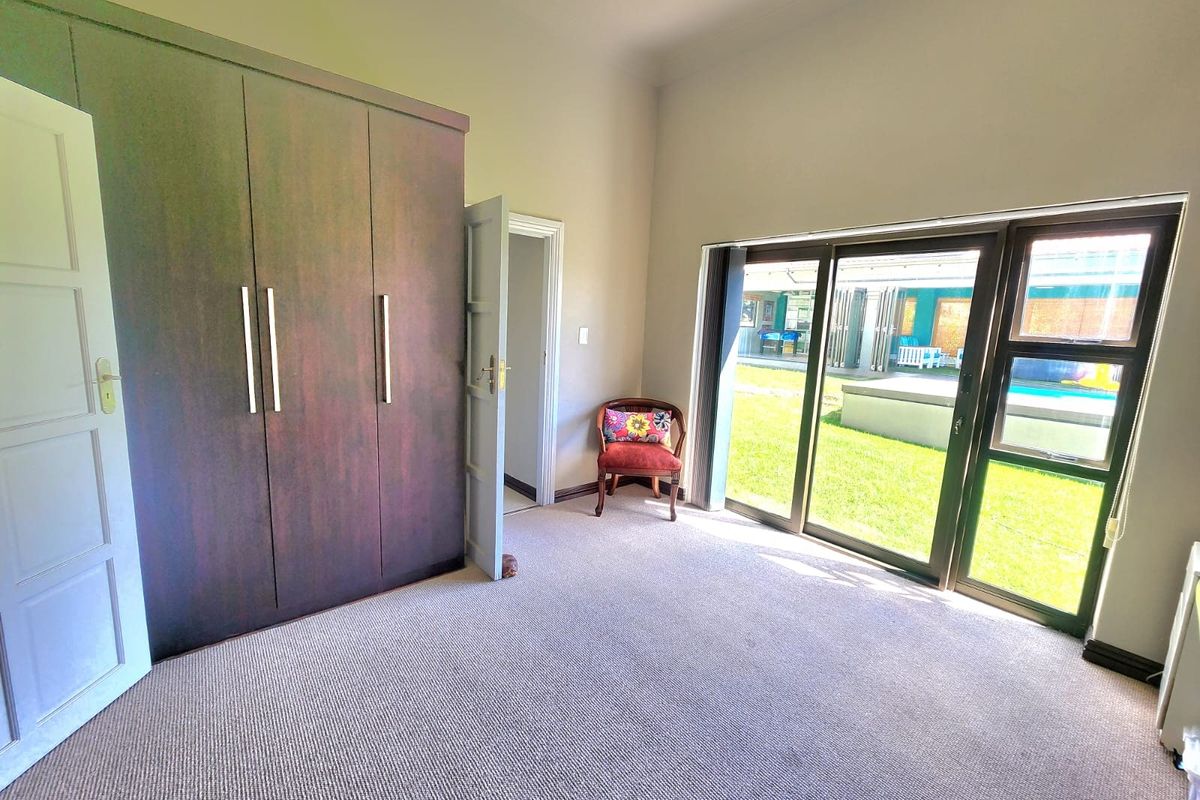 A bright bedroom featuring built-in cupboards, neutral carpeting, and large sliding glass doors providing direct access to the garden and pool area.
