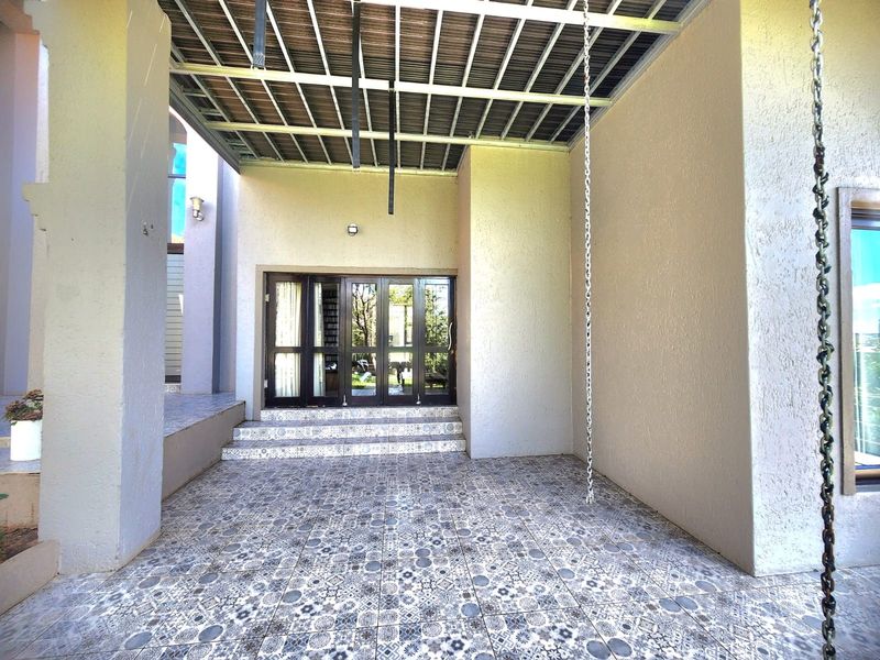 A covered patio area featuring decorative patterned floor tiles, an exposed metal roof structure, and glass sliding doors leading into the home.