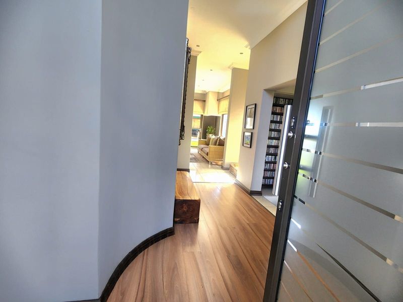 A welcoming entrance hall featuring modern laminate flooring, recessed lighting, and a stylish frosted glass door leading into the home's living areas.