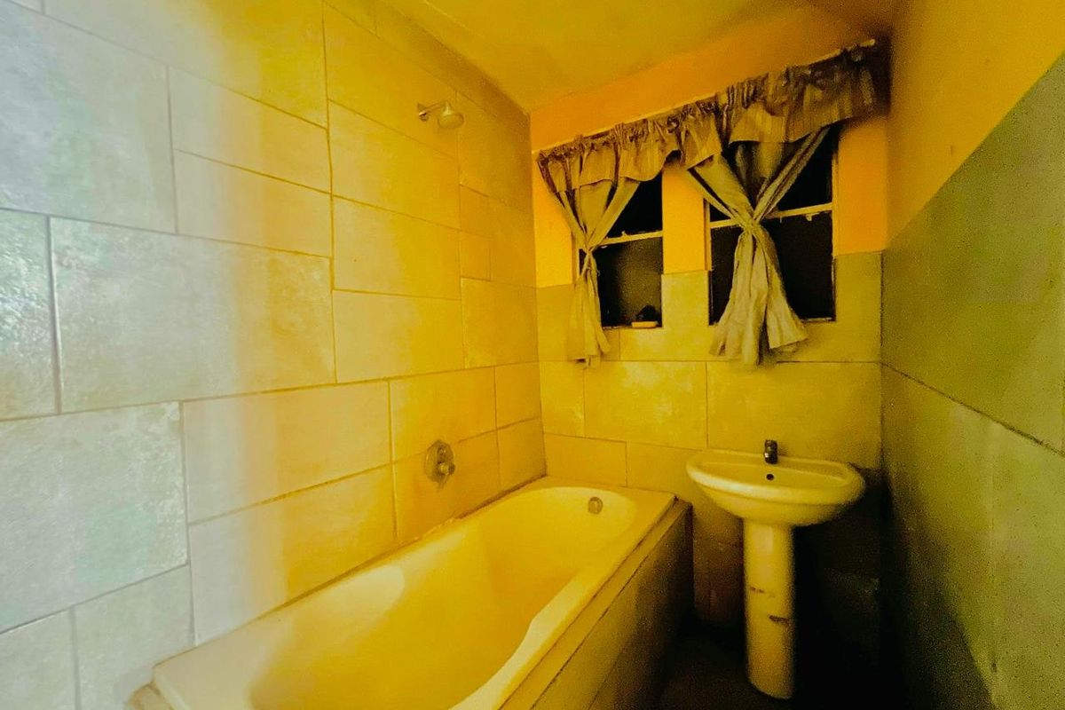 A dated bathroom featuring a built-in bathtub, pedestal sink, and wall tiling, requiring modernization to improve its aesthetic appeal and functionality.