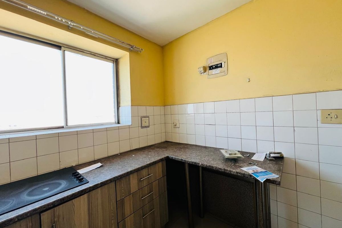 A compact kitchen featuring built-in cabinetry, a laminate countertop, an integrated electric hob, and tiled splashbacks, requiring cosmetic updates.