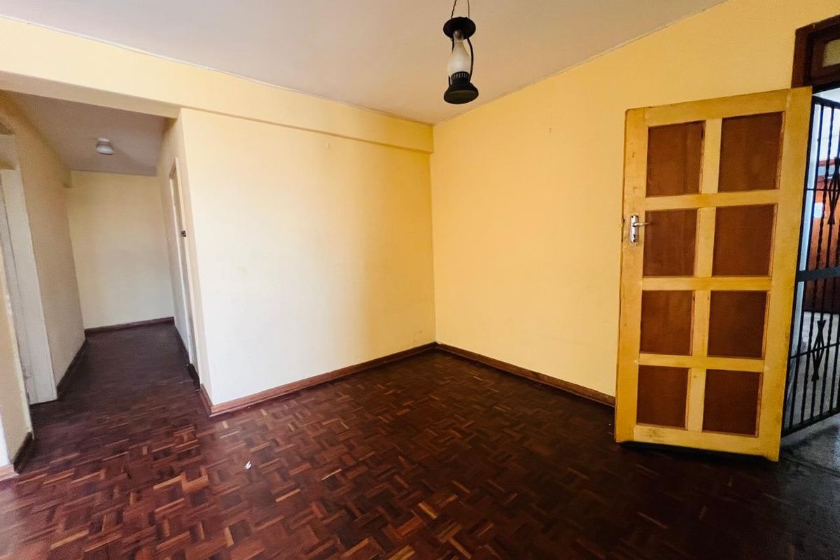 An empty living area featuring traditional parquet flooring, a timber panel door, and an adjacent hallway leading to further living spaces.