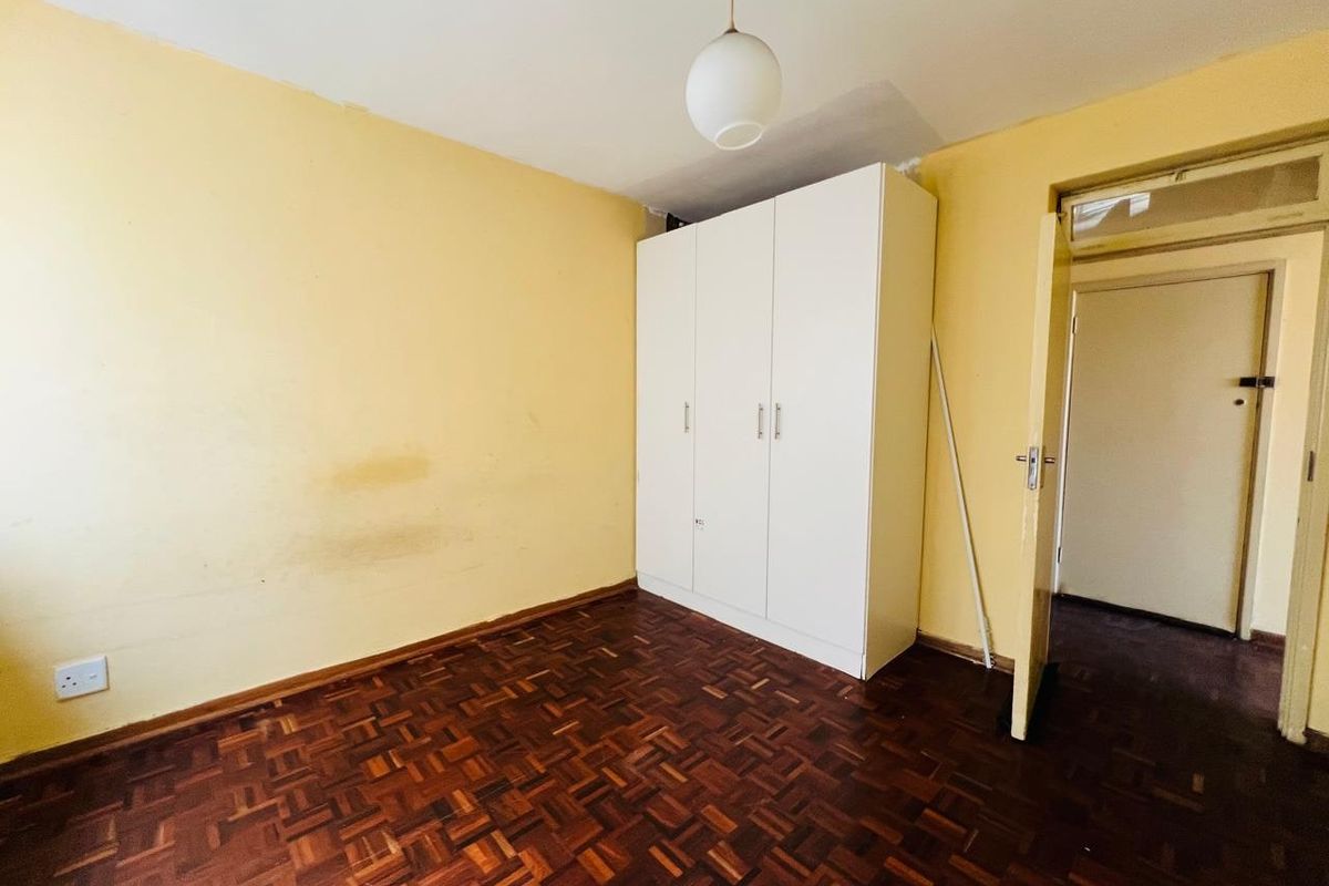 A bedroom featuring parquet flooring and a built-in wardrobe, requiring cosmetic updates to the wall finishes.