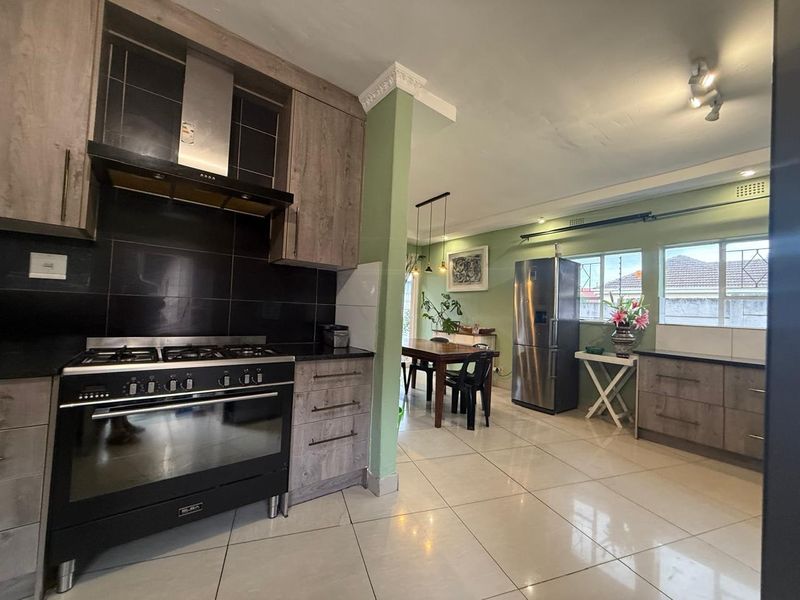 Open-plan kitchen and dining area featuring modern wood-finish cabinetry, gas stove, extractor fan, and tiled flooring throughout.