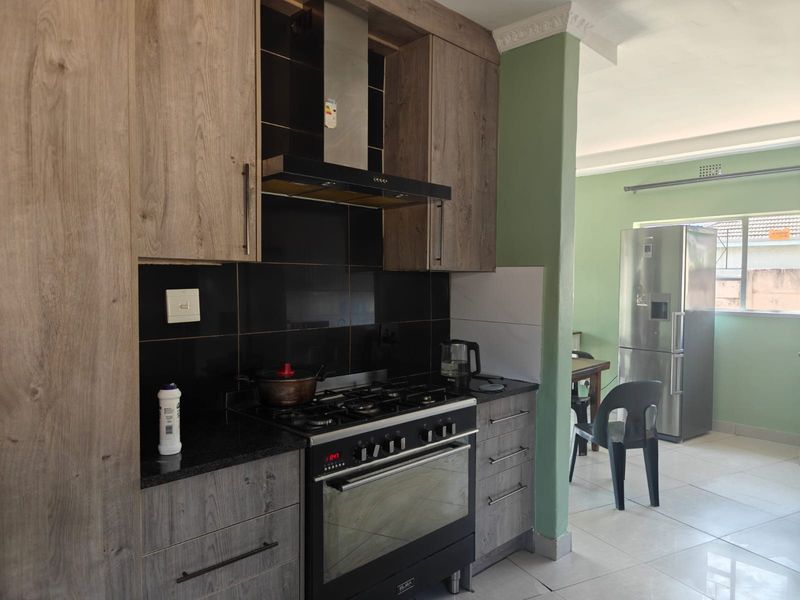 Modern kitchen featuring wood-look cabinetry, granite countertops, a gas hob with extractor fan, and tiled flooring, flowing into an adjacent dining area.