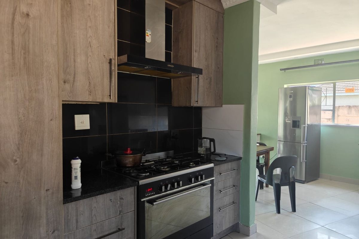 Modern kitchen featuring wood-look cabinetry, granite countertops, a gas hob with extractor fan, and tiled flooring, flowing into an adjacent dining area.