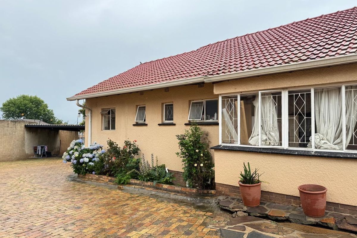 Rear exterior view of the house featuring a tiled roof, paved driveway, and security-fitted windows with a surrounding brick boundary wall.