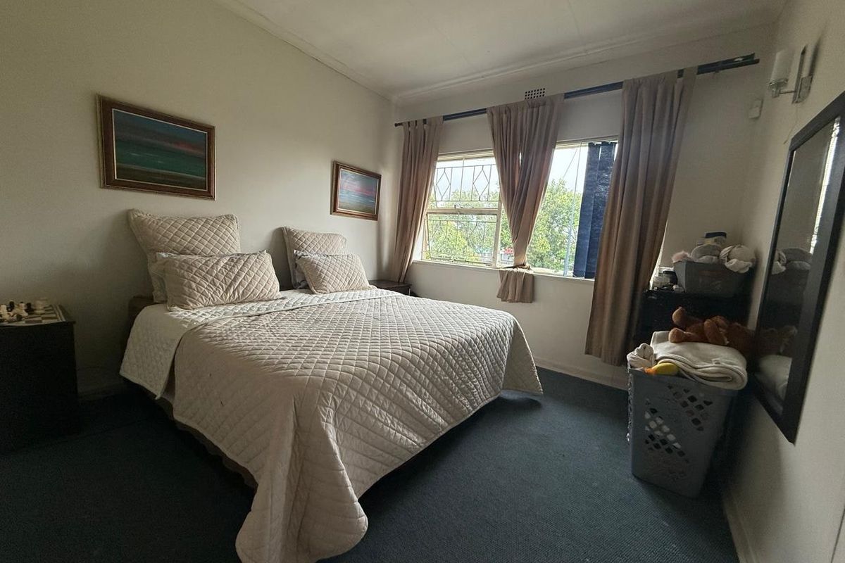 A standard bedroom featuring carpeted flooring, security bars on the window, and fitted curtain rails.
