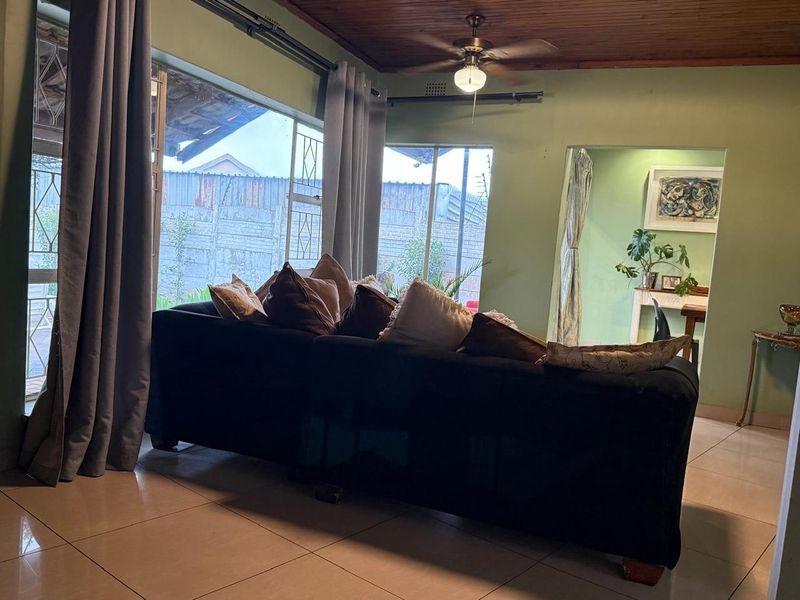 A living room featuring tiled flooring, a timber ceiling with a fan, and large windows with security bars overlooking the exterior.