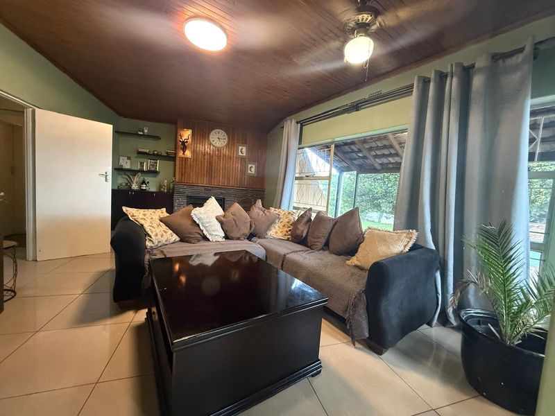 A living room featuring a timber ceiling, tiled flooring, and a brick fireplace, with direct access to an outdoor patio area.