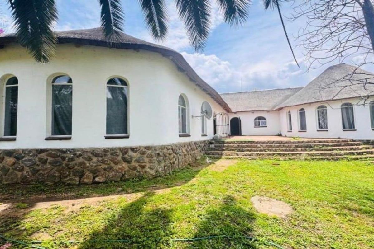Rear view of a unique house featuring a thatched roof, stone-clad base, and multiple arched windows opening onto a paved patio area.