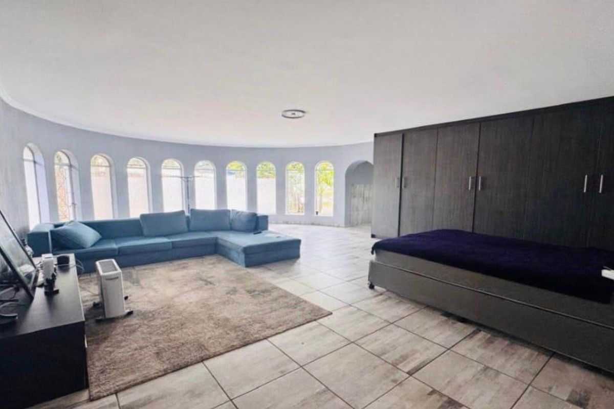 Spacious bedroom featuring large built-in wardrobes, tiled flooring, and a unique curved wall with multiple arched windows providing natural light.