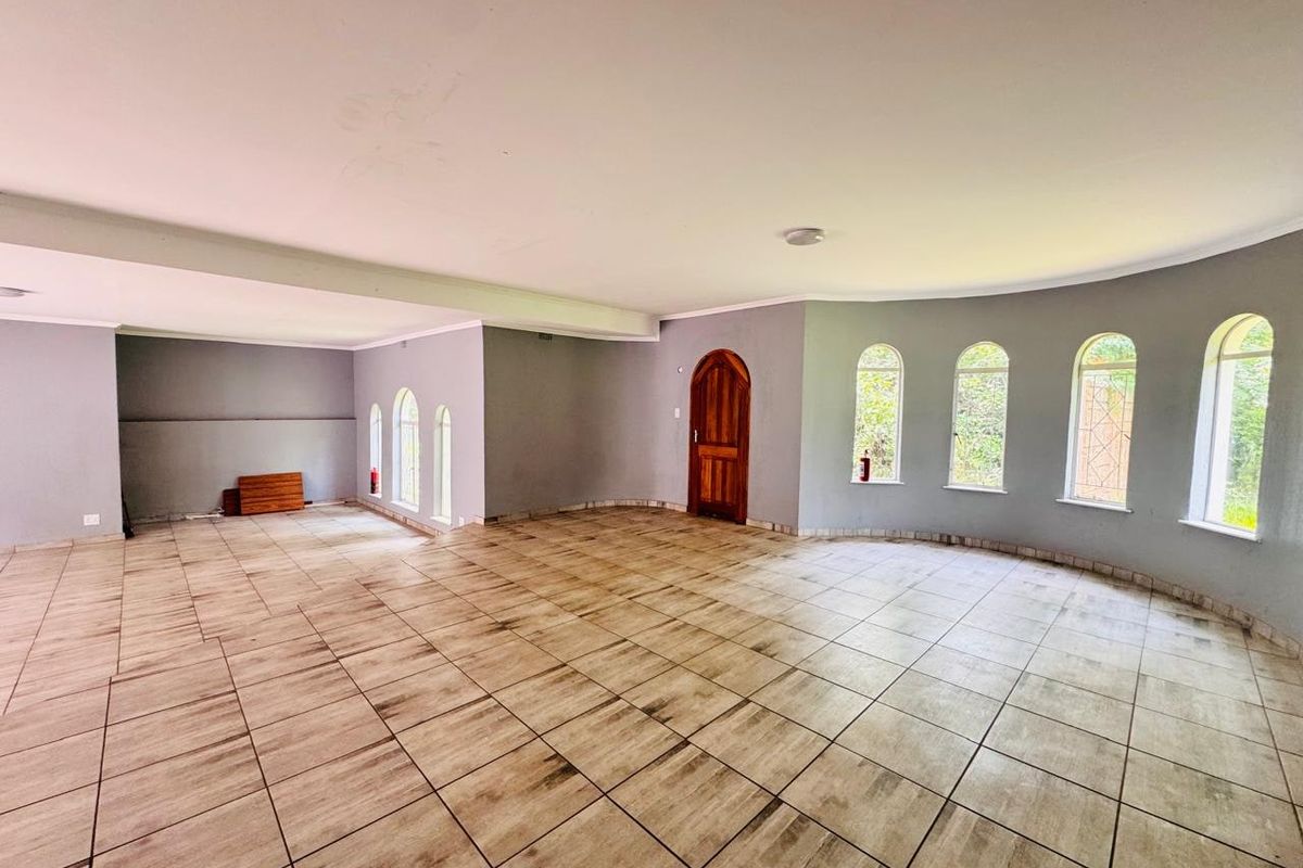 Spacious, open-plan living area featuring neutral grey walls, wood-look tiled flooring, and multiple arched windows providing natural light.