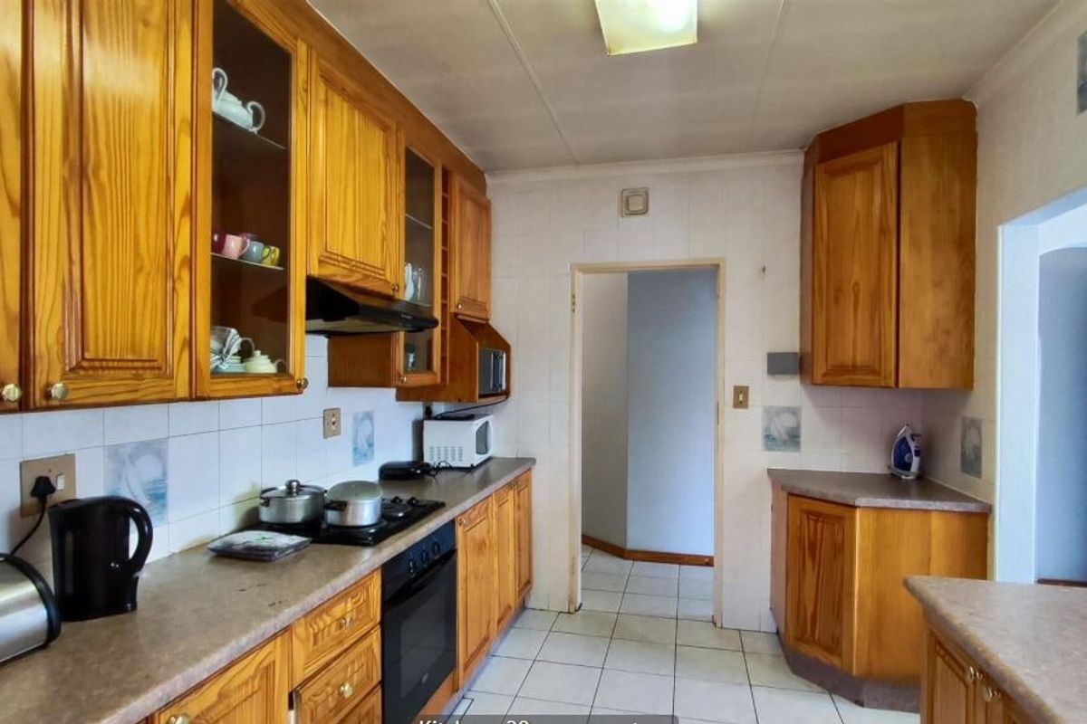 A functional kitchen featuring traditional wooden cabinetry, laminate countertops, built-in oven, hob, and tiled flooring with a practical layout.