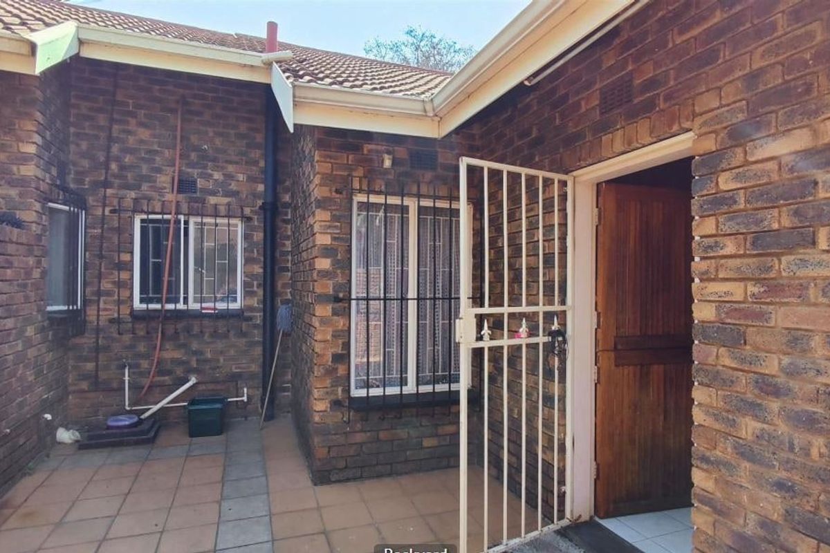 Rear exterior view of a townhouse featuring a face brick facade, tiled patio area, and secure entrance with a metal security gate.