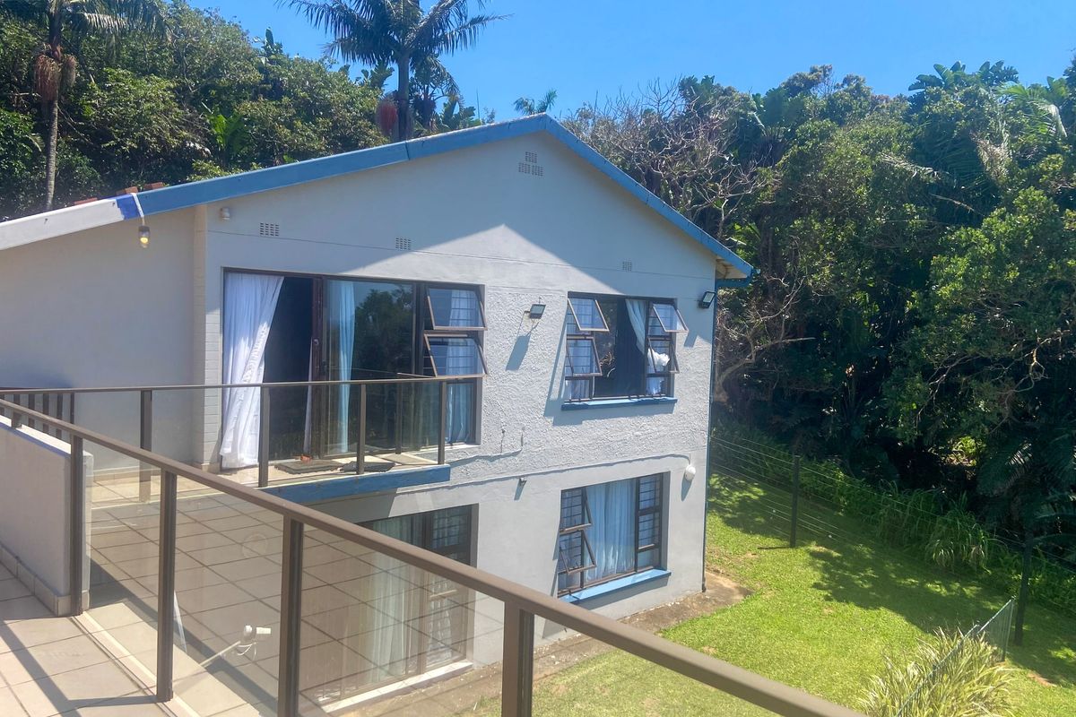 Rear view of a two-story house featuring a tiled balcony with glass balustrades, sliding doors, and casement windows overlooking a private garden.