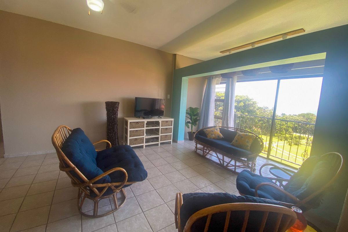 A bright living room featuring tiled flooring, a ceiling fan, and large sliding glass doors that open onto a balcony with scenic views.