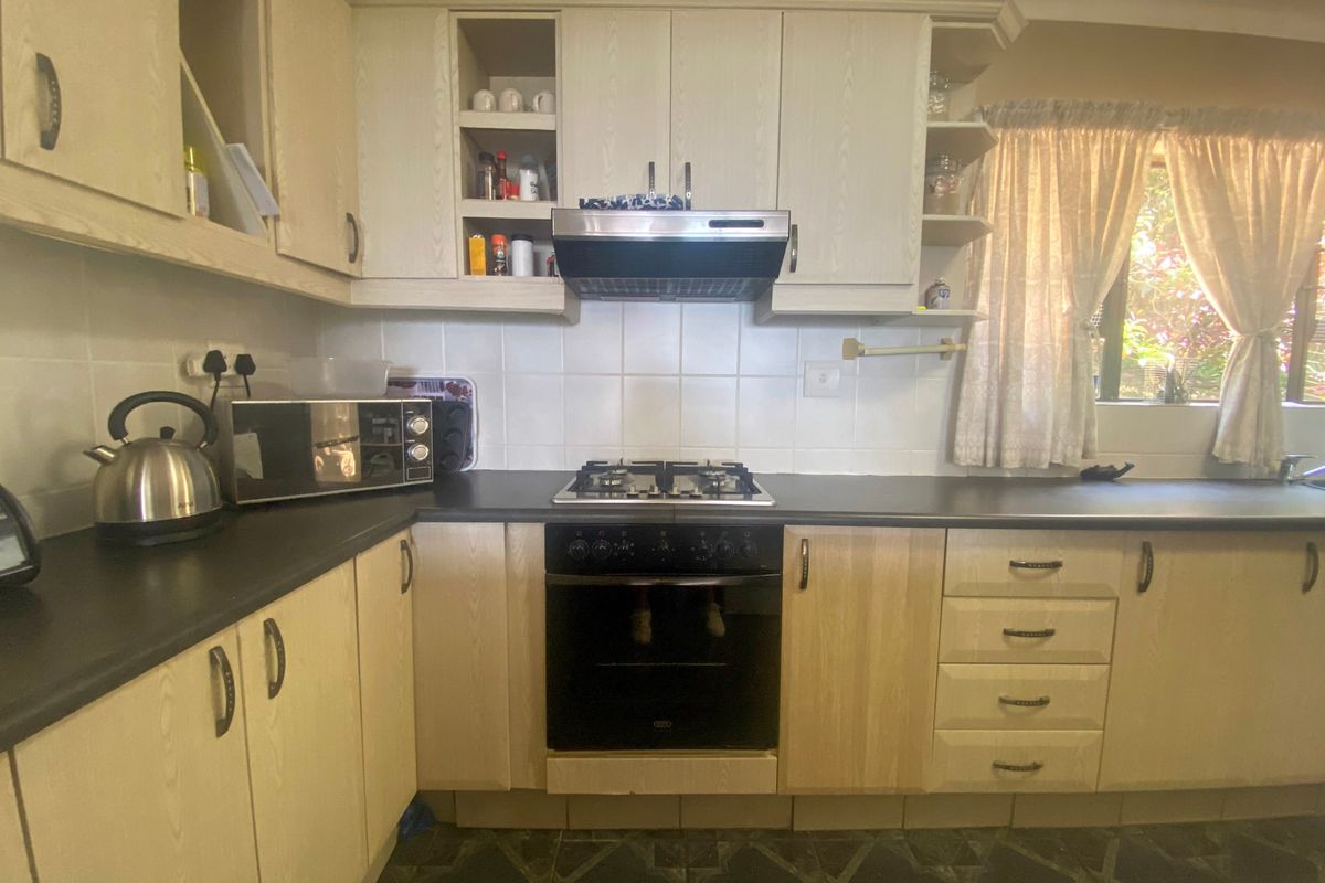 A functional kitchen featuring light wood-finish cabinetry, dark laminate countertops, a built-in oven with gas hob, and a tiled backsplash.