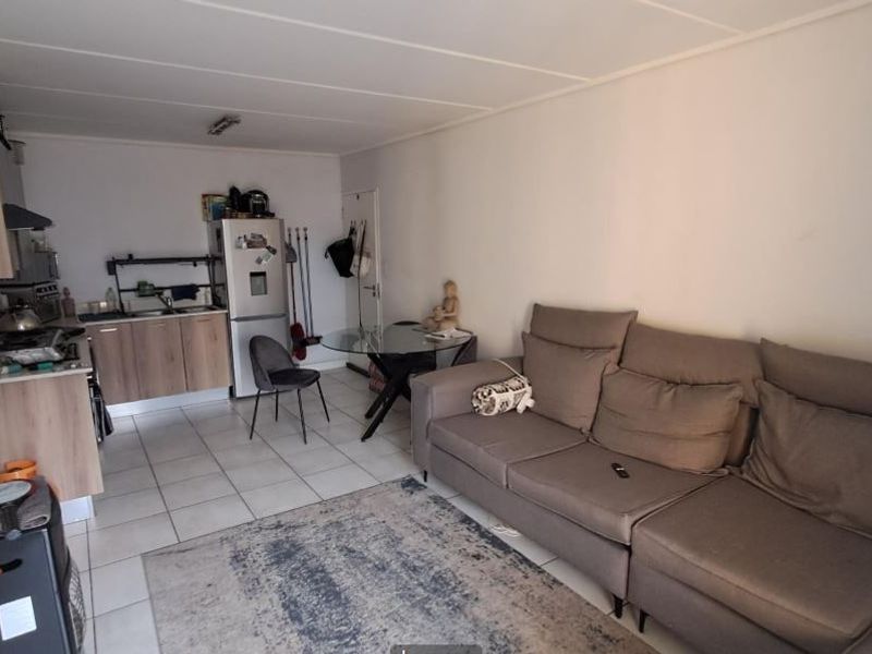 Open-plan living area featuring a compact kitchen with wood-finish cabinetry and tiled flooring, seamlessly integrated with the lounge space.